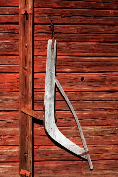 a very old agricultural tool made of wood hanging on a red barn