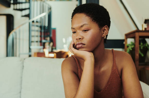 Young black woman sitting on her couch thinking with her hand under chin with copy space stock photo