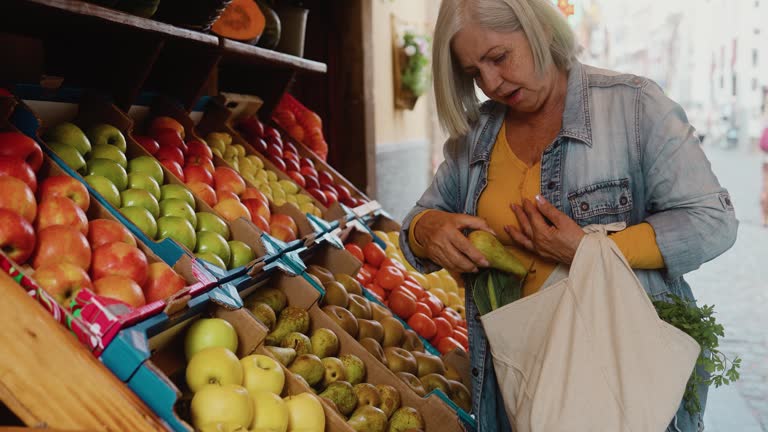 Happy senior woman buying fresh fruits at the market - Shopping food concept