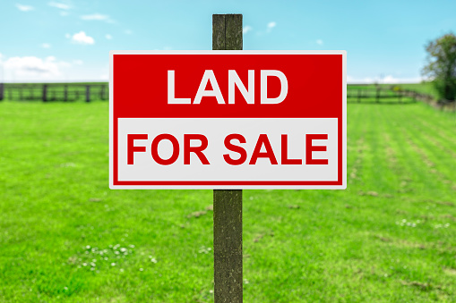 Land for sale sign in green grass field for housing development and construction background