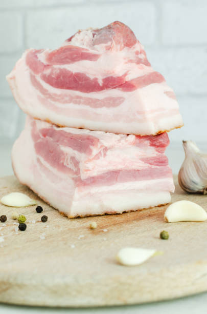 Fresh salted salo on a wooden board with garlic. Bacon. Concept Ukrainian traditional dish. Vertical orientation. Selective focus. stock photo