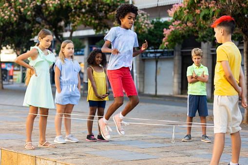 Group of kids playing with chinese jumping rope outdoors. Boys and girls having fun together.