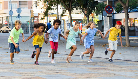 Happy children running together hand in hand through streets. Cheerful kids on summer vacation.