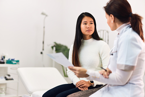 A pretty adult Asian female patient talking with a female doctor about a medical prescription.