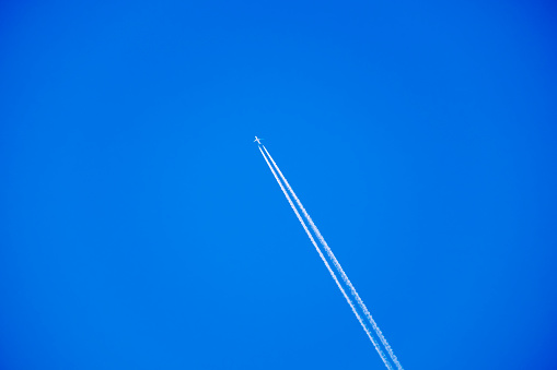 Distant passenger jet plane flying on high altitude through white clouds on blue sky leaving white smoke trace of contrail behind. Air transportation concept