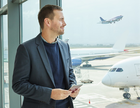 Business, window and man with passport, airport and excited for travel, thinking and international. Corporate, male leader and manager with ticket, check in and ready for flight, travelling and smile