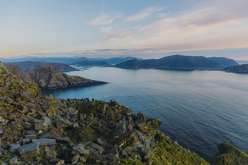 High-angle view of summer Scandinavian landscape with cliffs of the islands, snowcapped mountains and the ocean during sunset on Runde island, Western Norway