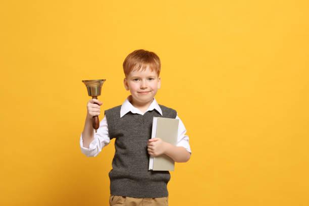 istock Pupil with school bell and book on orange background 1489124567