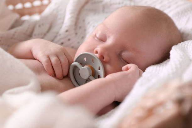 istock Cute newborn baby with pacifier sleeping on white blanket, closeup 1489125872