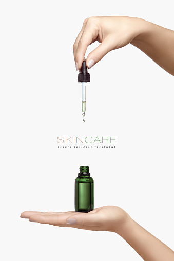 Graceful female hands holding a cosmetic dropper bottle with transparent fluid over a white background with copyspace for an advertising template