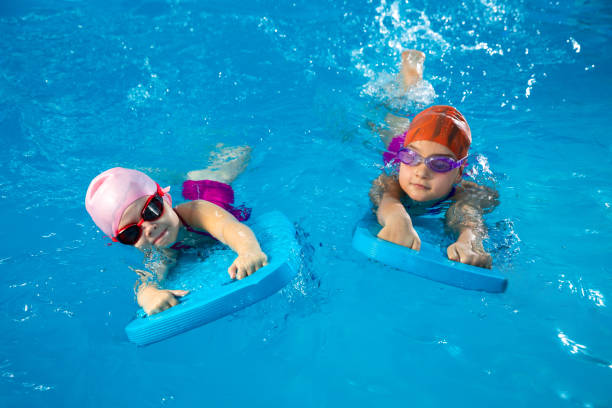 Two little kids learning how to swim in swimming pool using flutter boards stock photo
