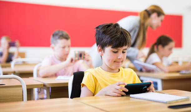 istock Schoolboy sitting at desk and using mobile phone during lesson 1489129110