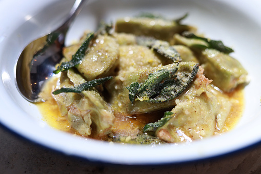 The close-up shot showcases a bowl of spinach agnolotti filled with mortadella and ricotta, accompanied by a lemon zest butter sauce, in a restaurant.