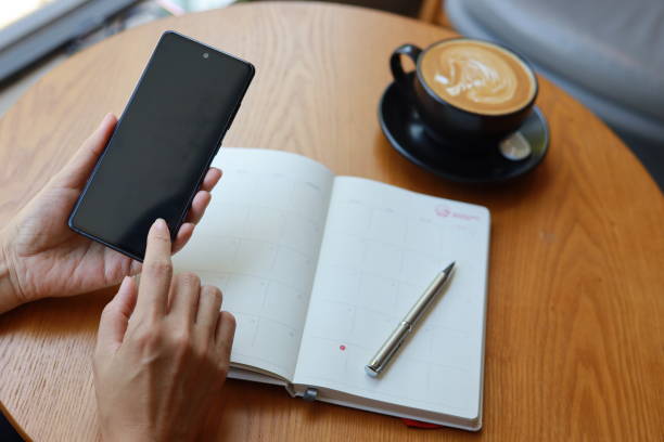 Cropped Image Of Asian Businesswoman Using Smartphone And Writing On A Note Pad, Working At Desk In Office