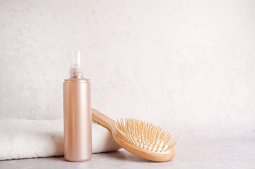 Still life with shampoo or lotion bottle and wooden hair brush with white towel on light concrete background, copy space. Hair care concept, natural cosmetics