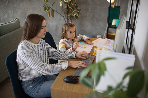 Mother Using A Computer While Her Daughter Is Drawing Next To Her Stock ...