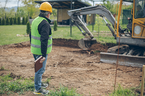Civil engeneer looking and coordinating an excavation process in homeowners backyard