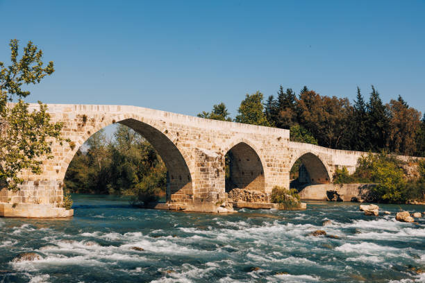 istock flowing river beneath the historic Aspendos bridge, surrounded by lush vegetation and the timeless beauty of this ancient landmark. 1489143896