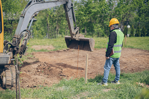 Civil engeneer looking and coordinating an excavation process in homeowners backyard