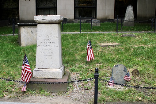 Boston, MA, USA, 9.13.21 - The top down, close up image of Paul Revere's original tombstone and the white memorial placed next to it. It's surrounded with American flags and other tributes.