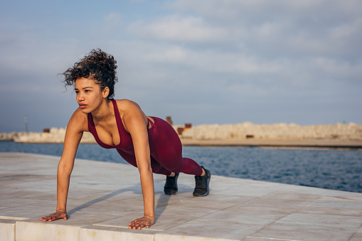 Beautiful fit woman doing push-ups outdoors by the sea alone.