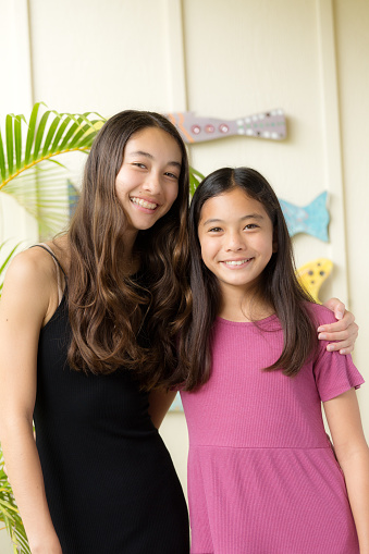 Portrait of two young Hawaiian teen adolescent girls in her home, looking at camera, smiling.