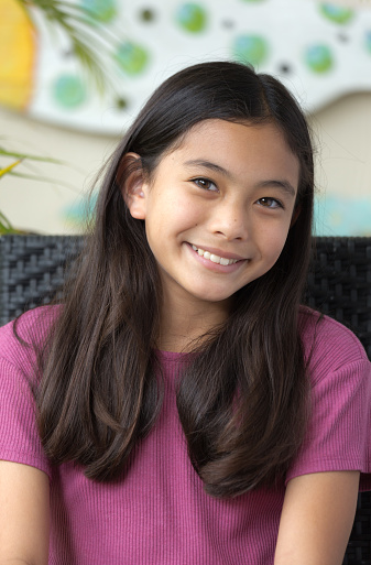 A young Hawaiian adolescent girl in her home, looking at camera smiling.