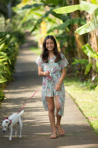 A young Hawaiian adolescent girl outdoor walking her dog, looking at camera, smiling.