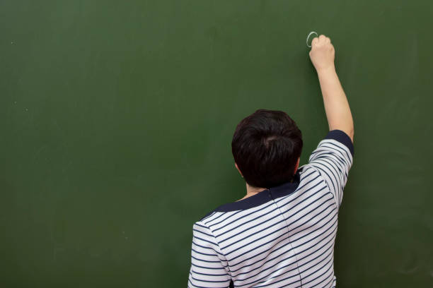 istock An elderly woman teacher writes with chalk on a blackboard.Back view. 1489155305
