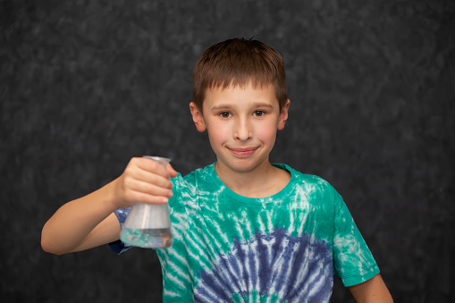 The boy holds a glass chemical flask in his hand.