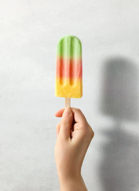istock Woman hand holding colorful fruit popsicle on light grey background 1489160345