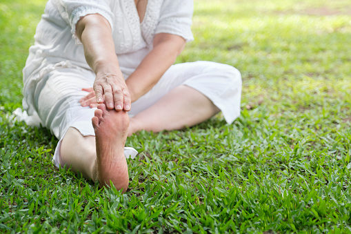 Unrecognizable woman in white clothes and barefooted doing stretching exercises outdoors in a park. Concepts: wellness, vitality, active and healthy lifestyle.