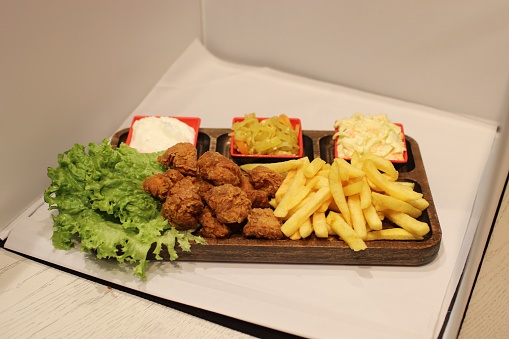 A wooden tray filled with French fries, fried chicken, and other snacks.