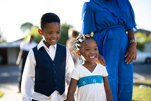 Smiling small boy with his happy baby sister walk beside their Mother up the pathway toward church