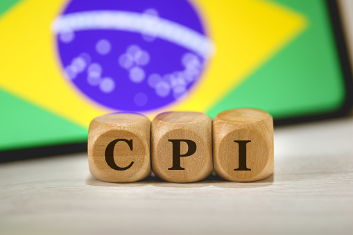 The acronym CPI for Parliamentary Commissions of Inquiry in Brazilian Portuguese written on wooden dice. In the background the flag of Brazil on the screen of a cell phone.
