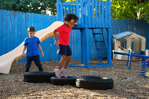 Two kids jumping and playing, leaping over old tires in the playground of her daycare