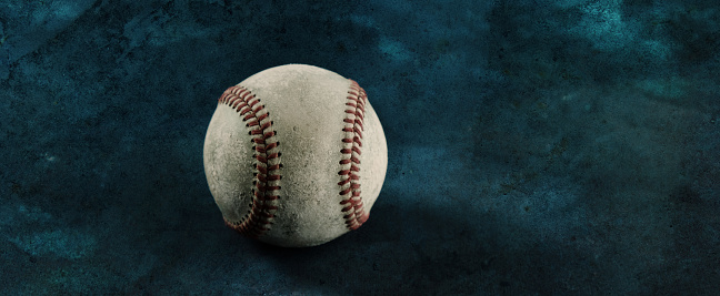 An old baseball on a rustic wood background. Extreme shallow depth of field with sharp focus on the center of the ball.