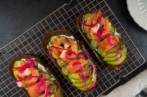 Scandinavian-style open-faced sandwiches (smorrebrod): Shrimp, smoked salmon, avocado, and cucumber on rye bread. Garnished with pickled red onion.\n.