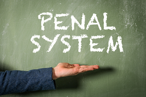 Penal System Concept. Text and a woman's hand on a green chalkboard background.