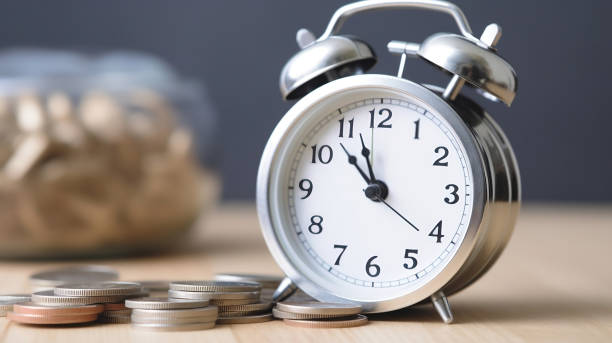Next to a clock is a pile of coins, symbolizing the phrase "time is money." Next to a clock is a pile of coins, symbolizing the phrase "time is money." moment of silence stock pictures, royalty-free photos & images