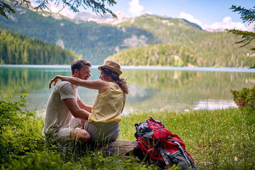 young adult caucasian couple hugging each other by the lake with beautiful view in front of them
