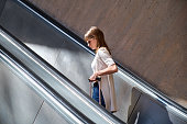 young girl in profile going up an escalator with a suitcase illuminated by the sun