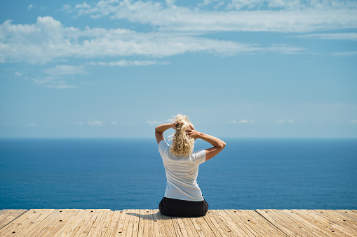 Adult beautiful woman rejoices in a warm day, blonde sits against the backdrop of a magnificent seascape, a journey through the Greek islands, a famous place for vacation and travel