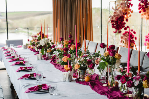 Luxury elegant table setting dinner with floral centerpiece in a restaurant. Decoration with pink and orange flowers roses, candles, fruits. Plate, dishes, glasses, forks, napkins. Decor rustic style.