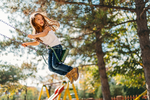 Cheerful little girl having fun swinging in the park