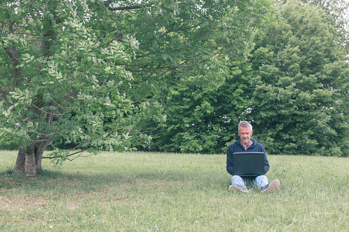 Adult man is using laptop for his work outdoors in green environment nature on springtime day.