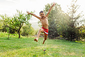 Child having fun refreshing with garden sprinkler