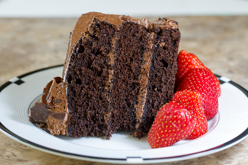 A slice of chocolate cake with chocolate frosting and fresh strawberries