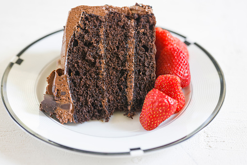 A slice of chocolate cake with chocolate frosting and fresh strawberries