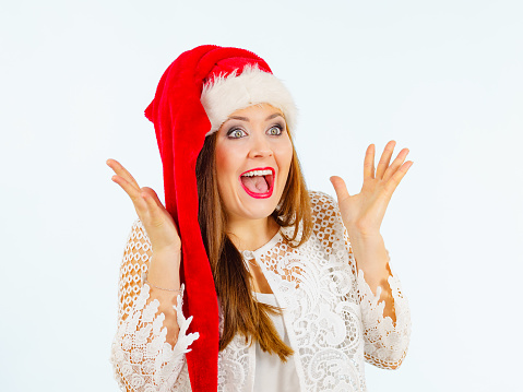 Woman wearing santa claus hat surprised shocked face expression, on blue. Christmes time.